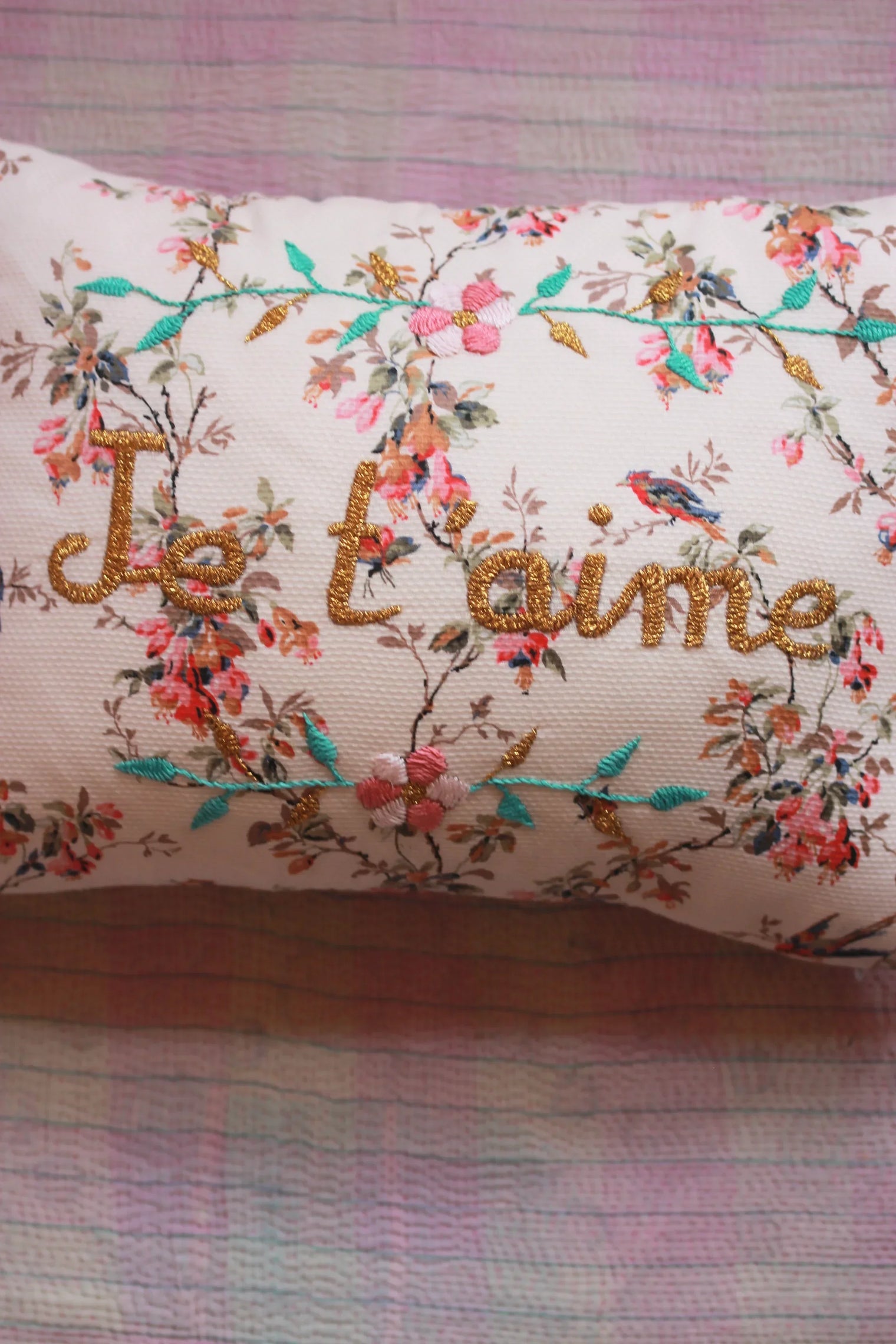 Embroidered pillow with floral pattern, birds, and gold "I love you" text on a pastel quilt