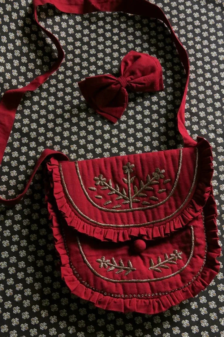 Red embroidered shoulder bag with matching bow hair accessory on floral fabric background