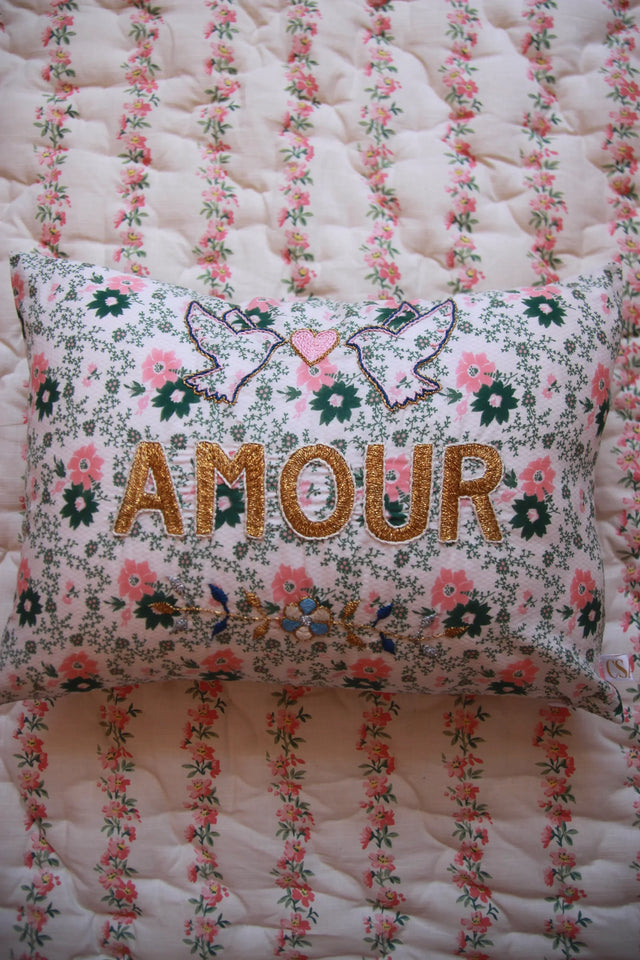 Floral embroidered pillow with gold 'AMOUR' text, doves, and heart on quilted bedding
