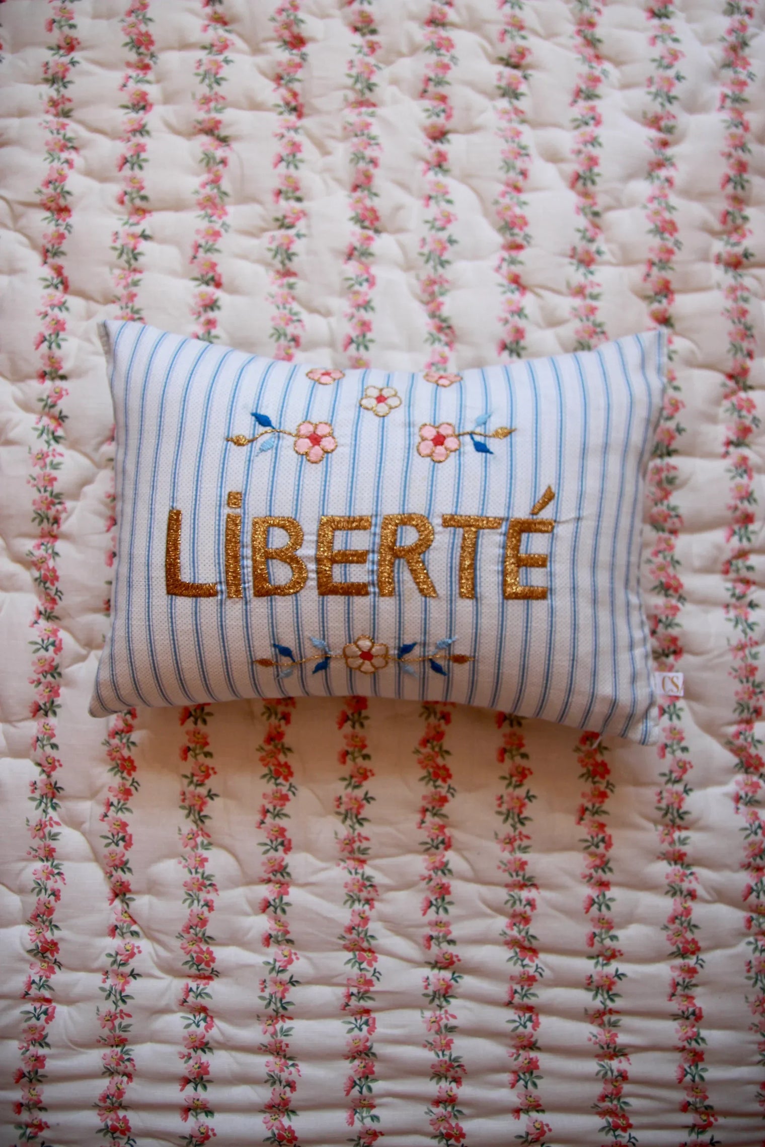 Striped decorative cushion with "LIBERTÉ" embroidery and floral design on a floral quilt