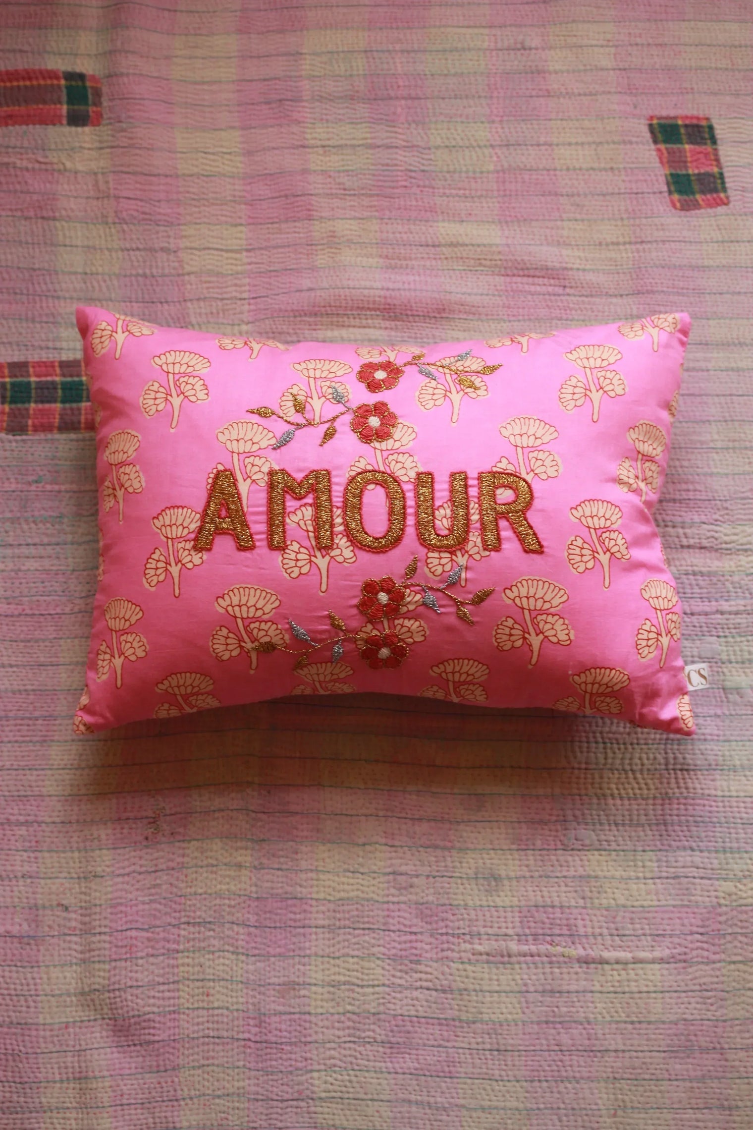 Pink embroidered decorative pillow with 'Amour' text and floral pattern on pink quilt
