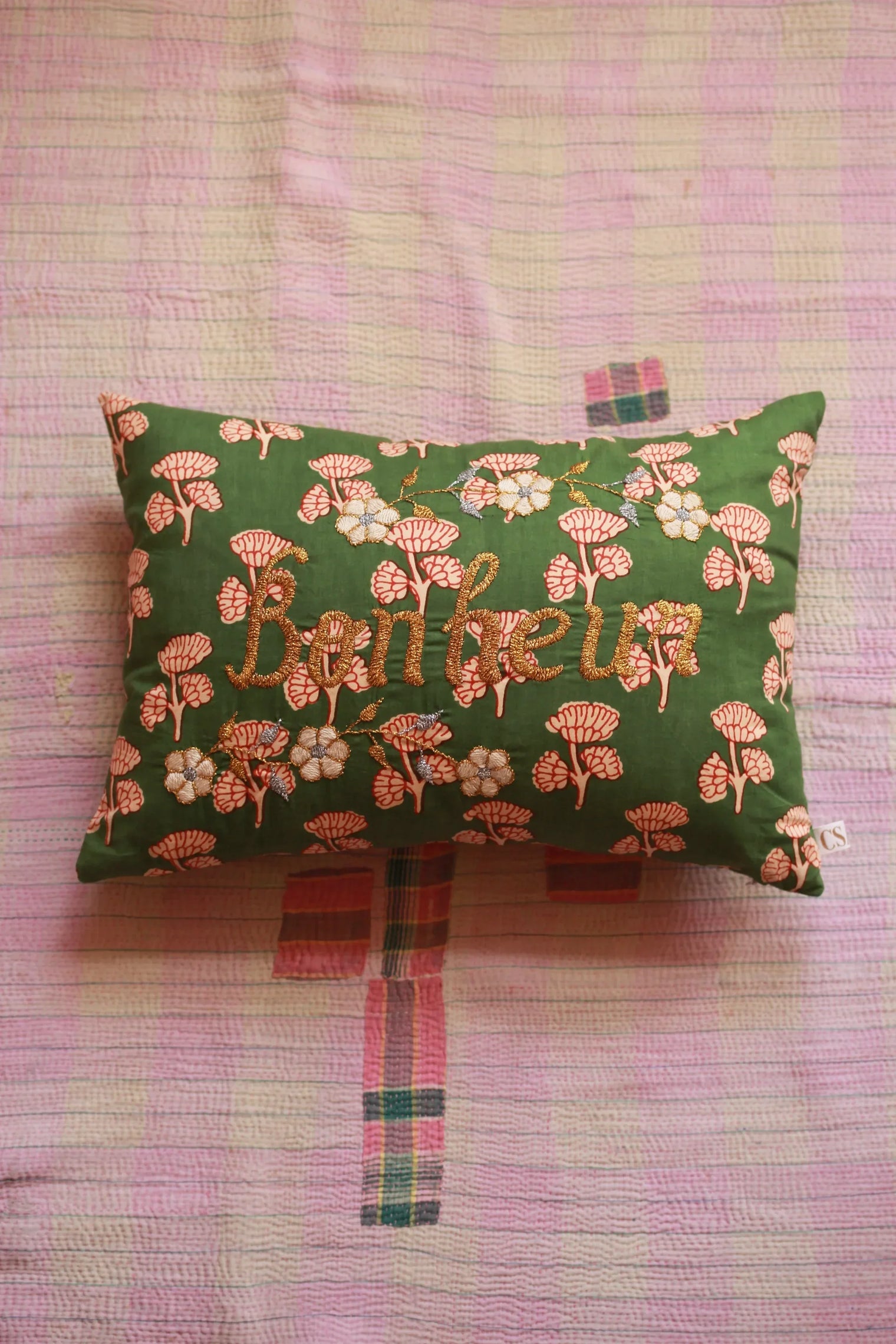 Green floral embroidered cushion with "happiness" on a pink quilted bedspread