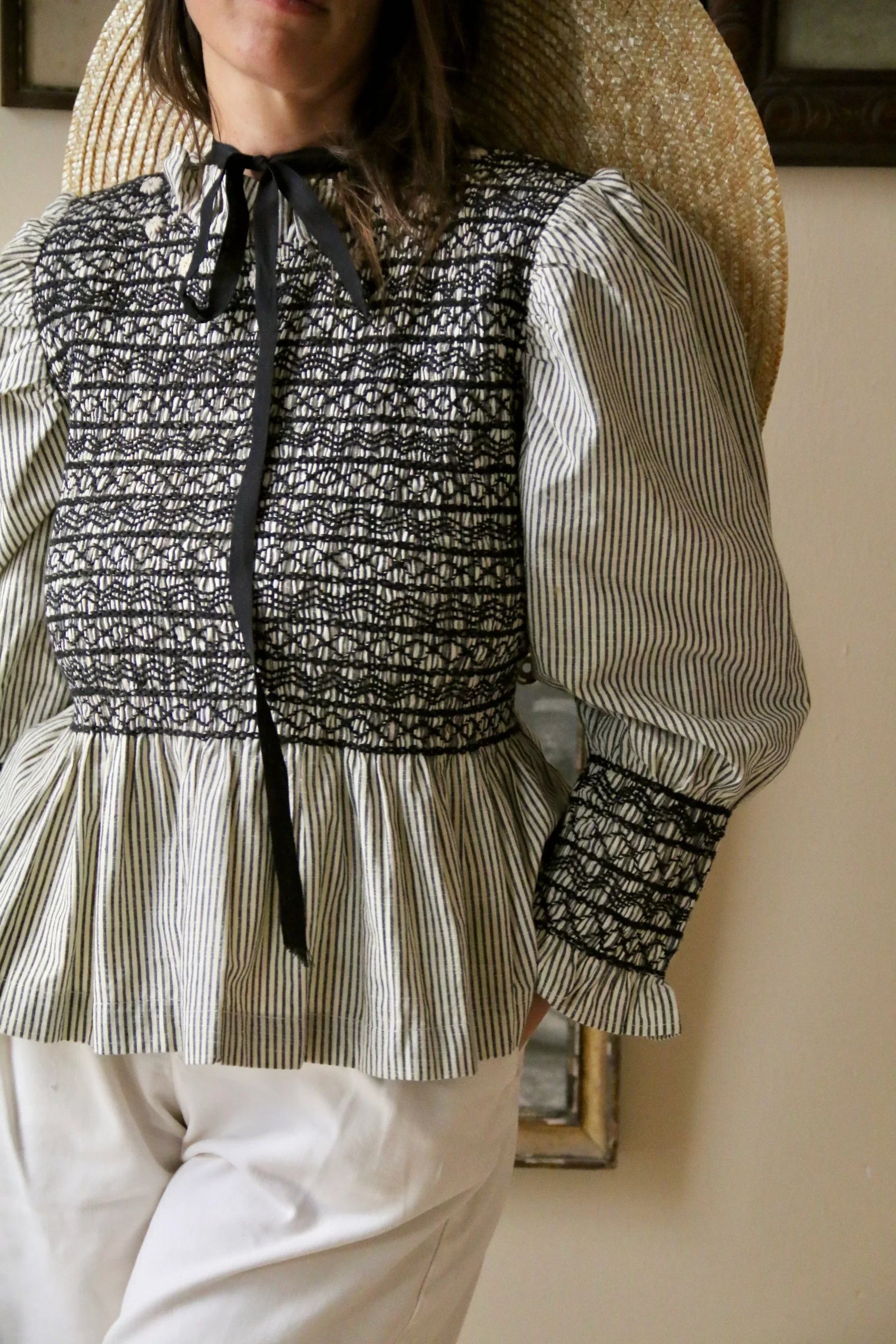 Woman wearing a striped, long sleeve smocked blouse with a ruffle collar and black ribbon tie