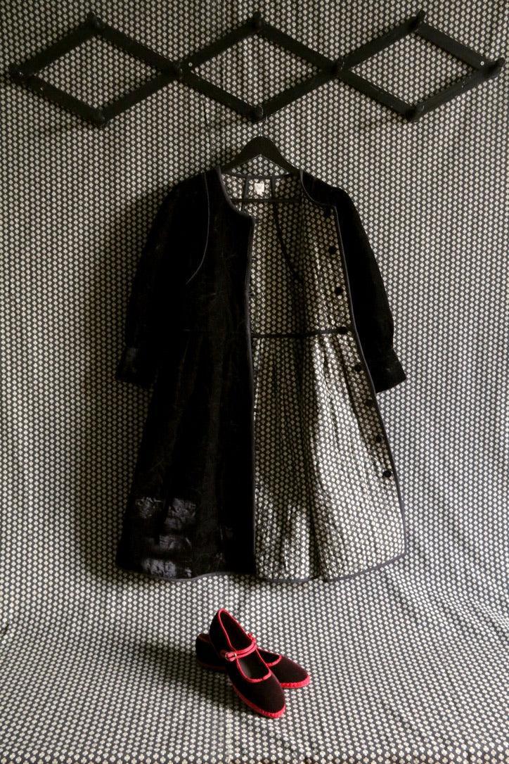 Children’s black coat with patterned lining and red-trimmed black shoes on a geometric background