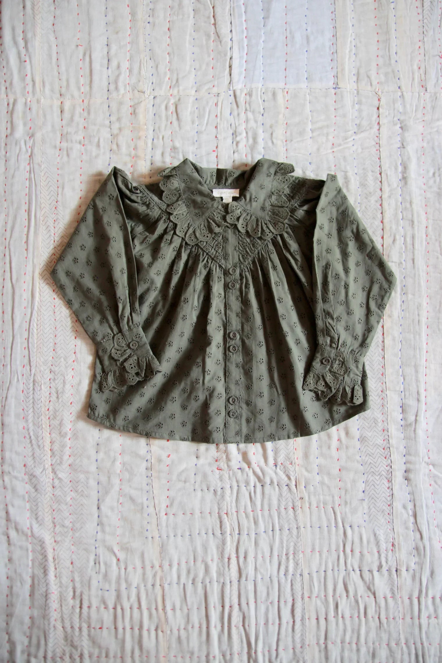 Green eyelet-embroidered children's blouse with lace collar and cuffs on a quilted background