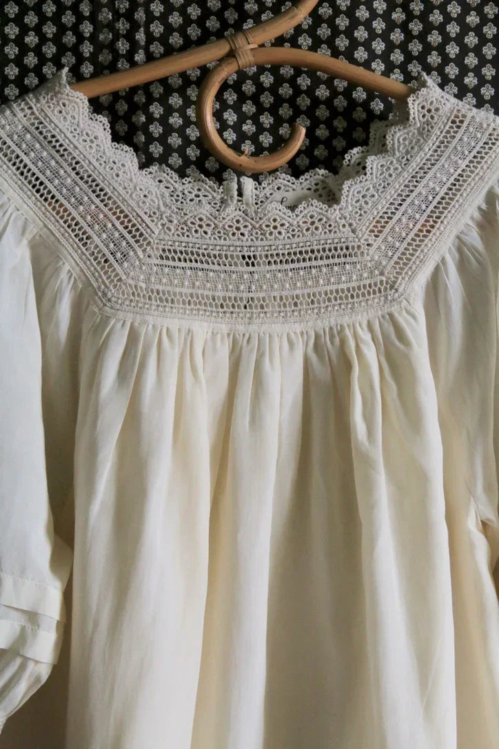 Cream-colored dress with lace yoke and puff sleeves on a hanger, vintage style