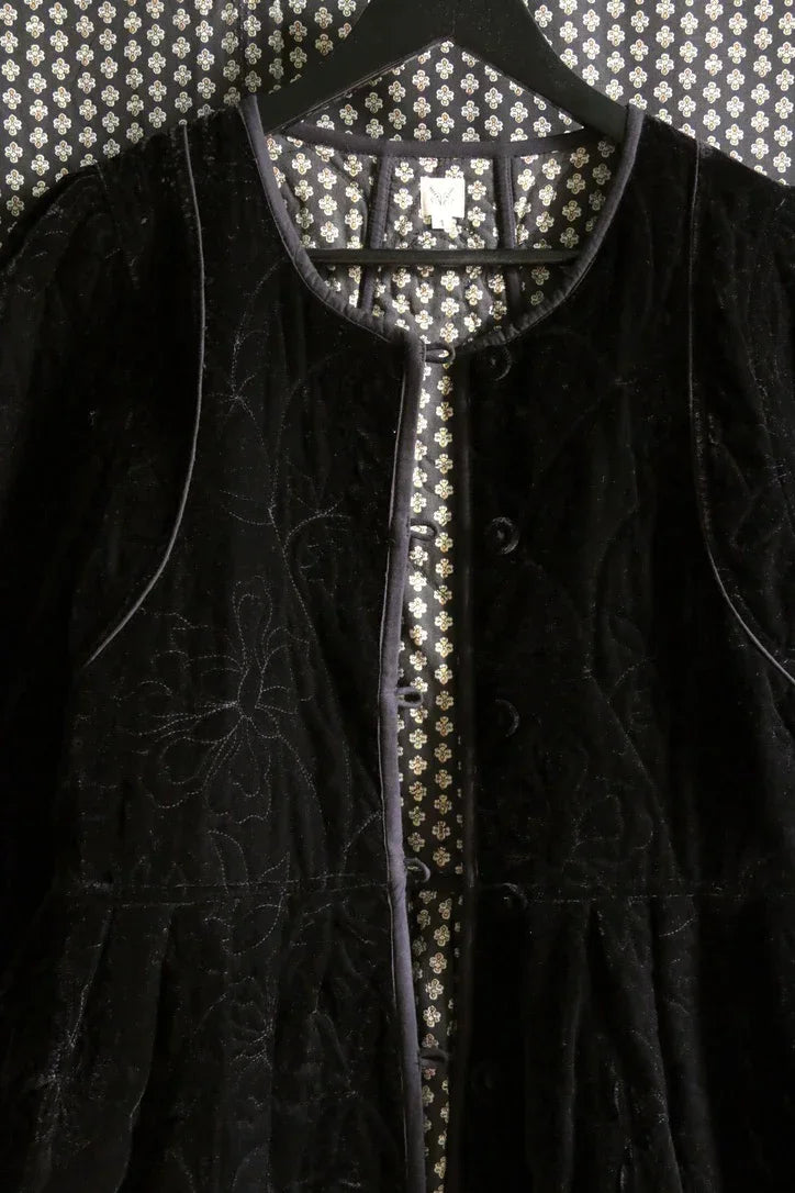 Black velvet jacket with floral embroidery on a hanger against patterned wallpaper
