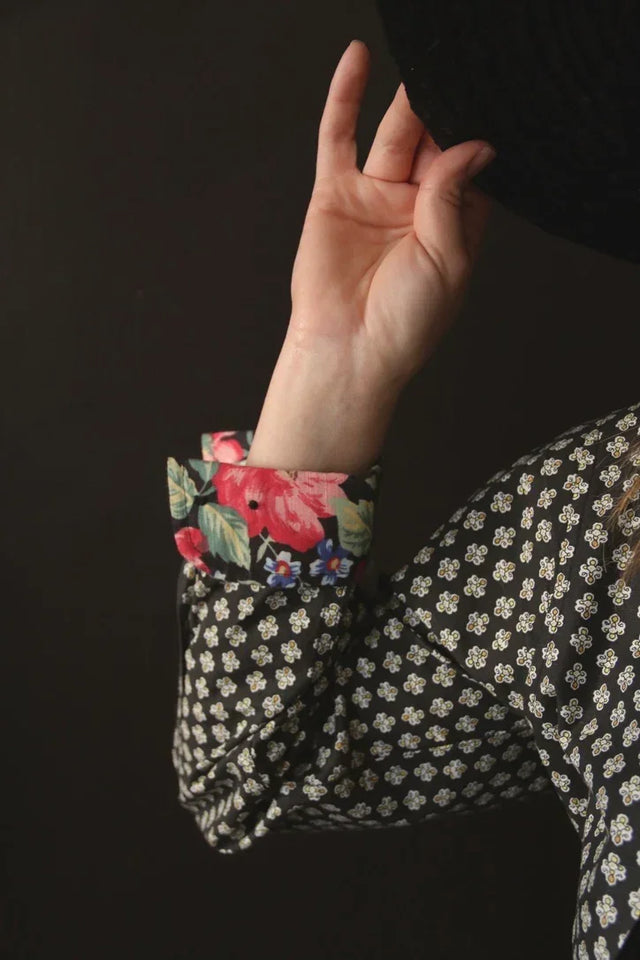 Black patterned shirt with floral print cuffs, hand adjusting a dark hat