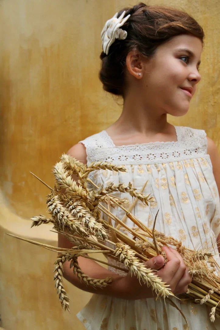 Girl in white embroidered dress holding wheat bouquet against warm yellow background