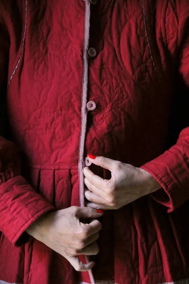 Woman buttoning a quilted red jacket with floral stitching details
