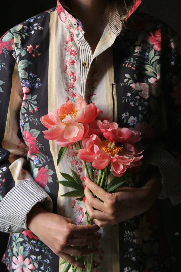 Person in floral patchwork shirt holding pink peony flowers, close-up view.