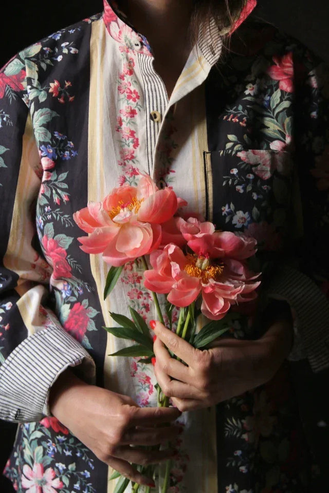 Person in floral patchwork shirt holding pink peony flowers, close-up view.