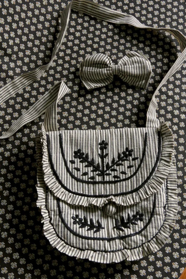 Striped fabric shoulder bag with floral embroidery and matching hair bow on floral background