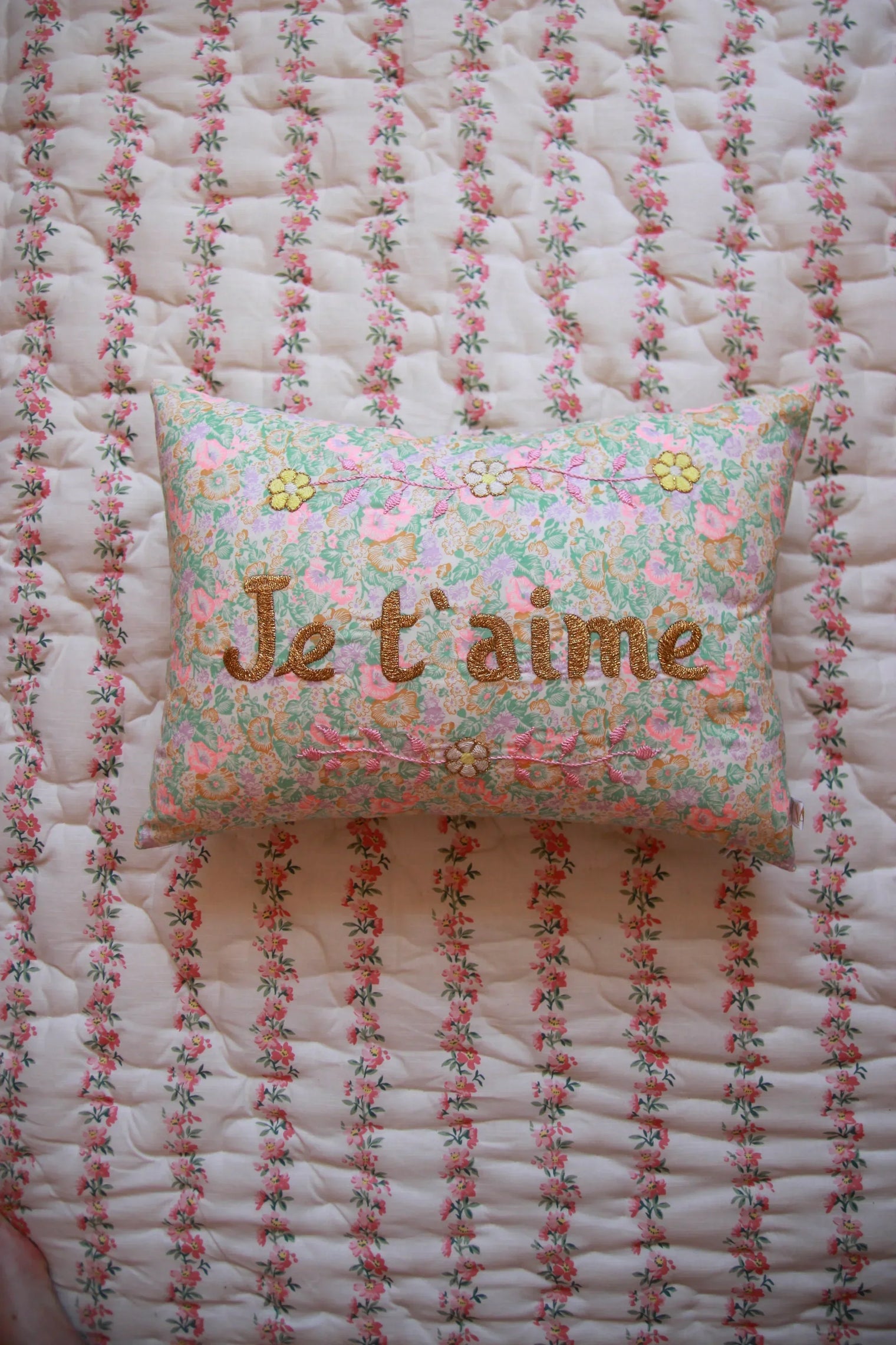 Floral embroidered pillow with "I love you" text on a quilted floral bedspread