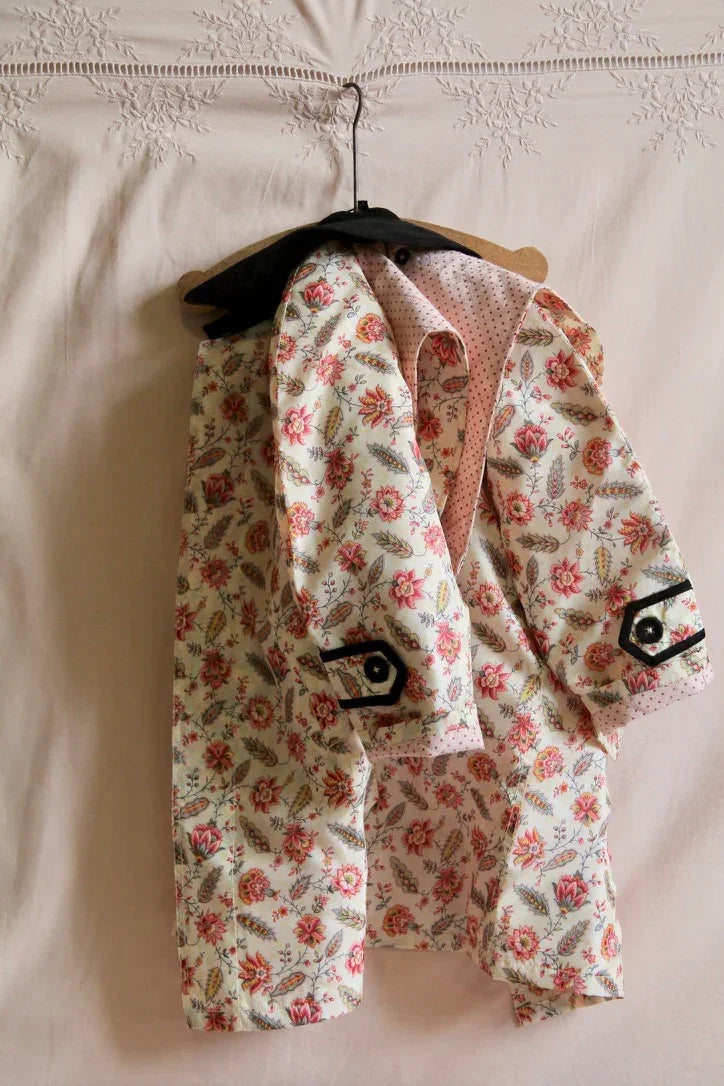 Floral print children's jacket with pink lining and black buttoned cuffs on a hanger.