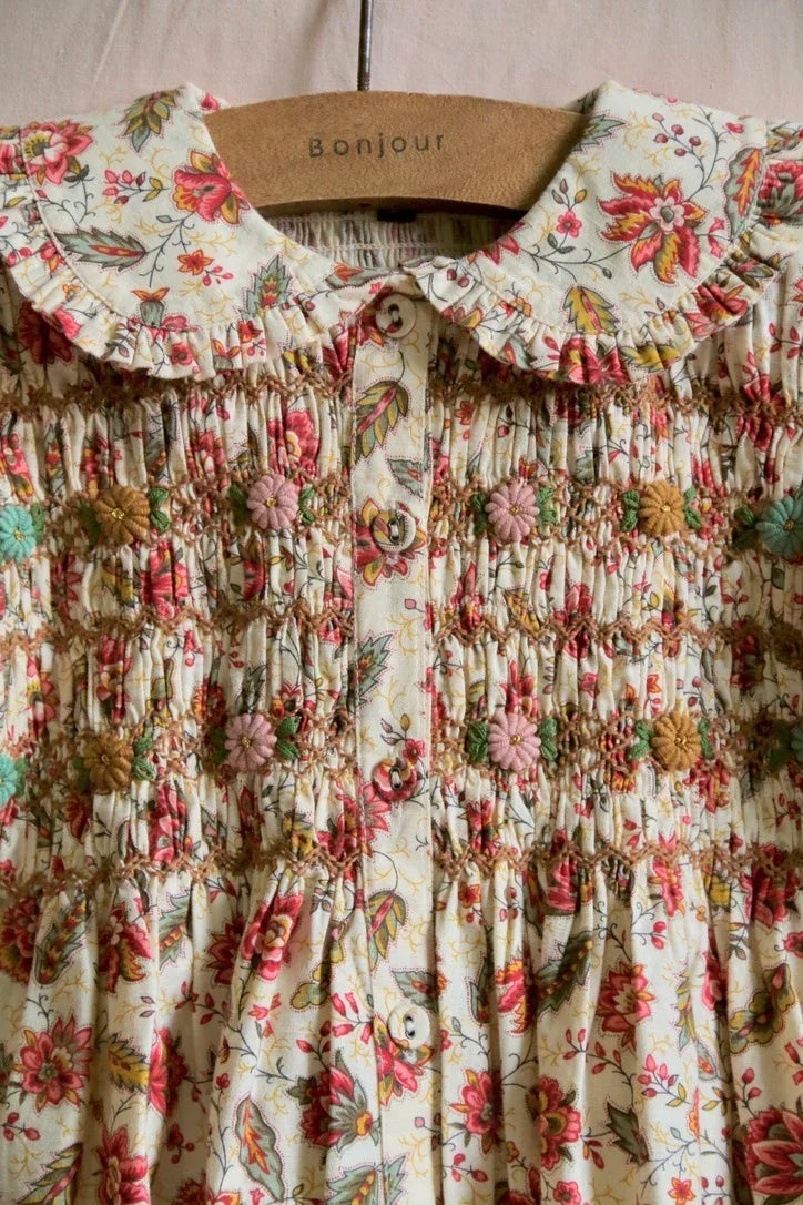 Floral embroidered children's dress with smocked bodice and Peter Pan collar on hanger