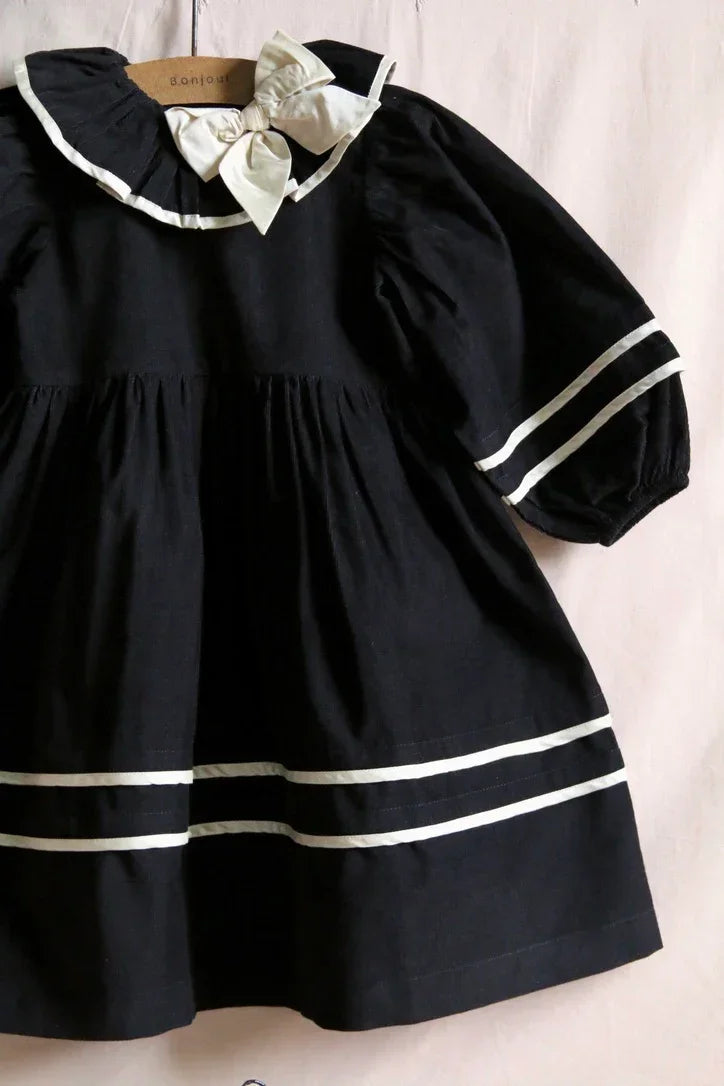 Black long-sleeve cotton dress for children with white trim and a large bow collar.
