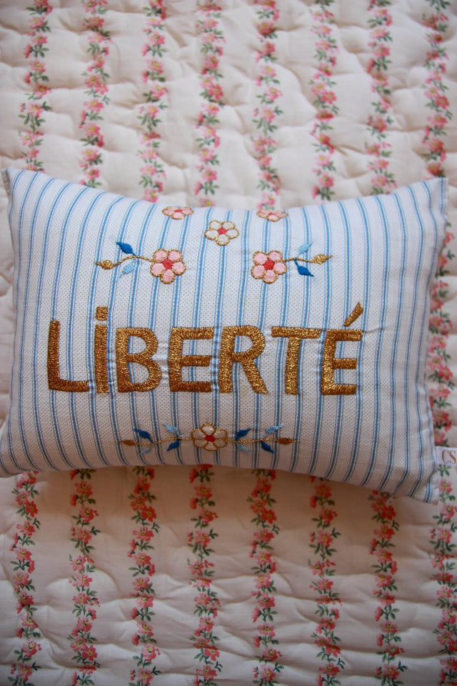 Striped embroidered pillow with 'LIBERTÉ' and floral designs on a floral quilted blanket