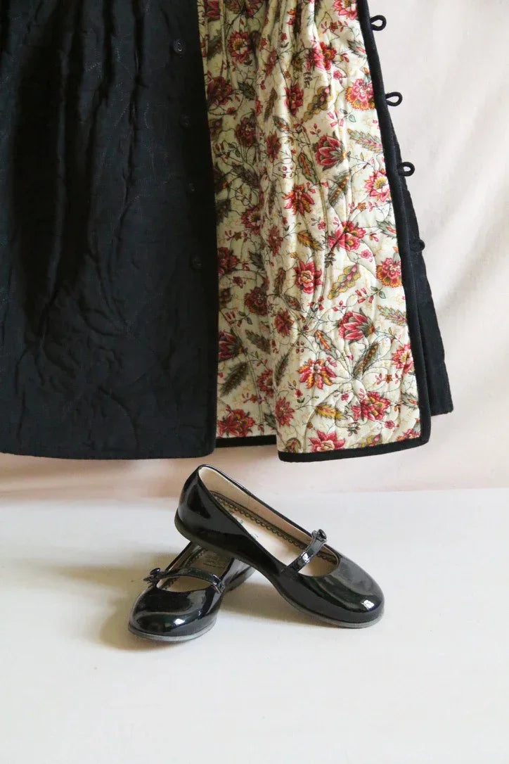 Black quilted coat with floral lining and black patent Mary Jane shoes on white background