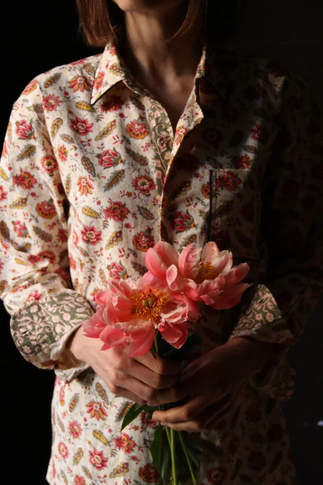 Woman wearing floral print shirt holding pink peonies in soft natural light