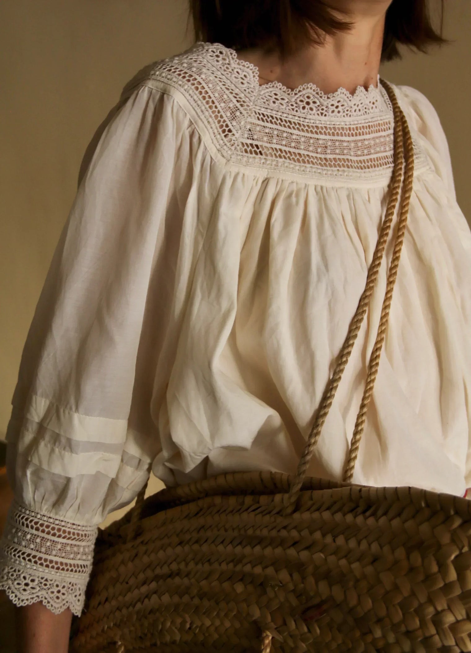 Woman wearing a cream lace-trimmed blouse and carrying a woven straw bag