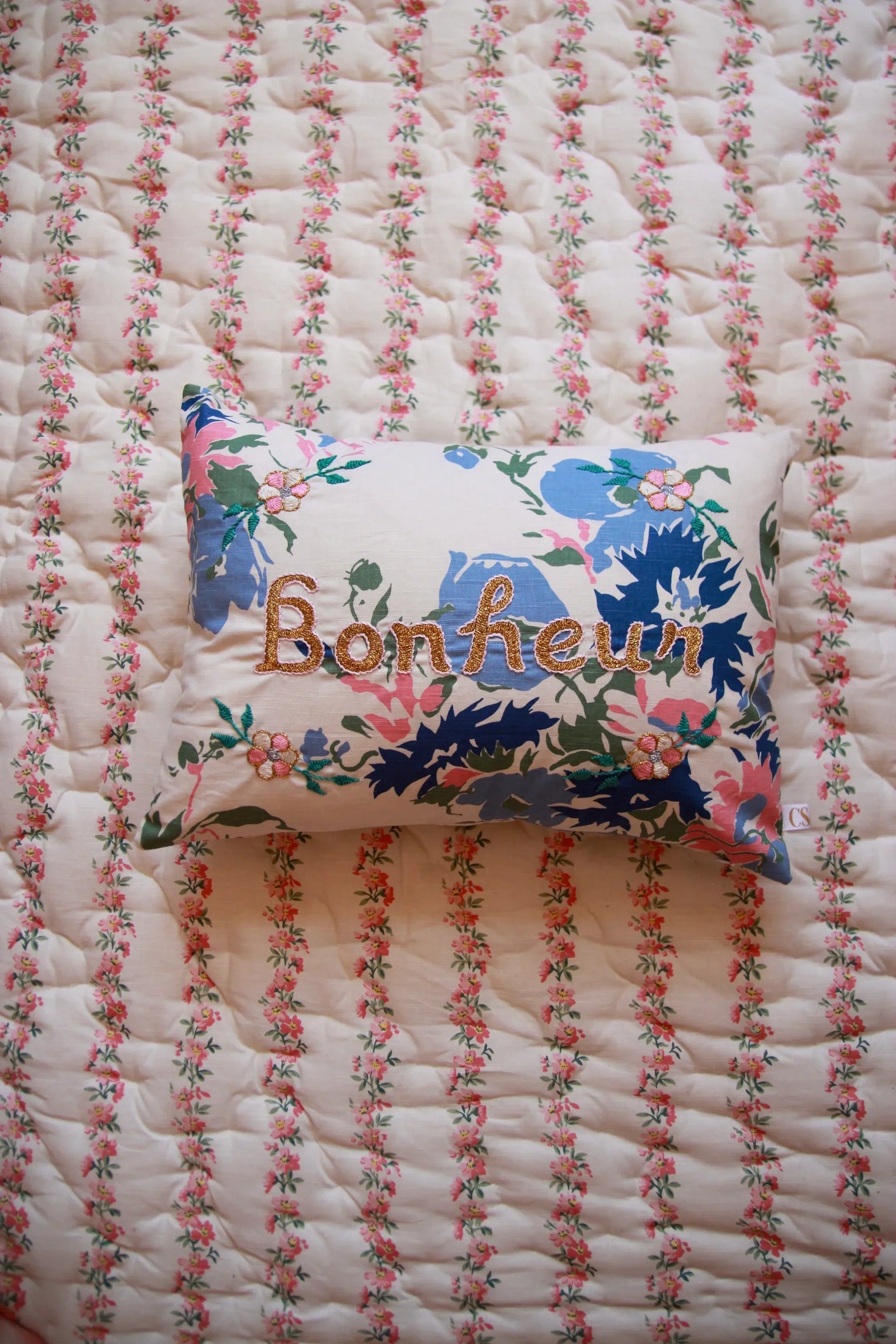 Floral embroidered cushion with "Happiness" text on a quilted floral bedspread