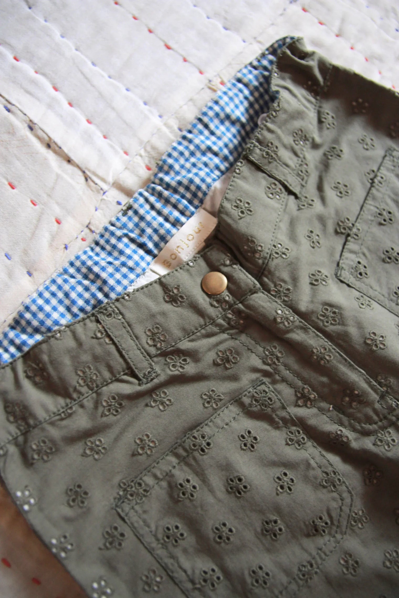 Olive green embroidered children’s shorts with blue gingham lining on a quilted fabric background