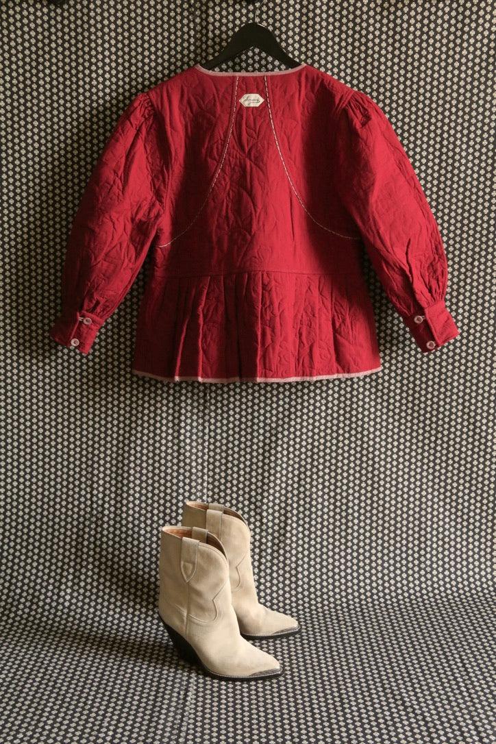 Red quilted children's jacket on hanger with beige suede boots, geometric background