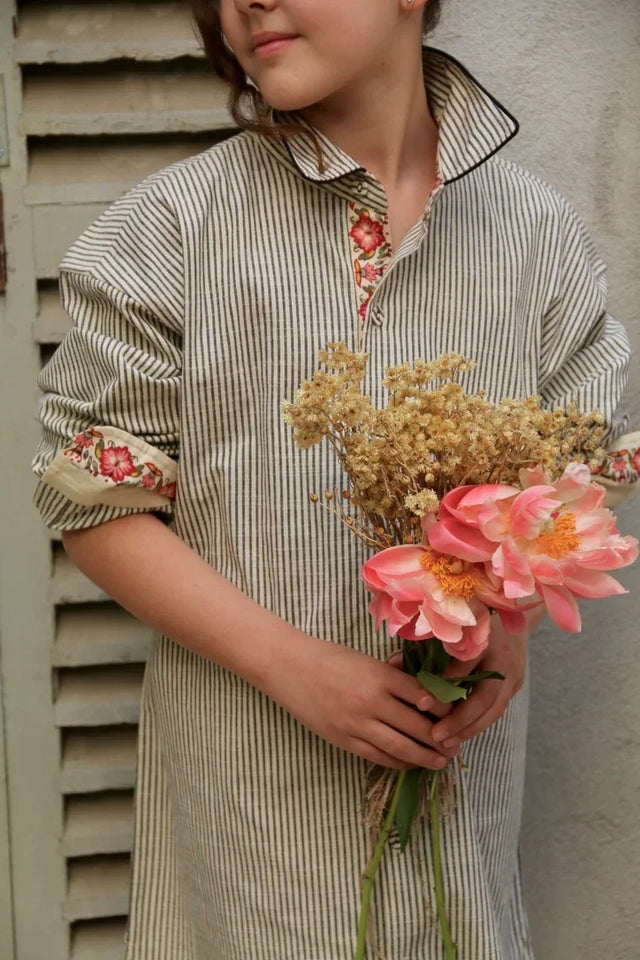 Child in striped shirt dress with floral trim holding bouquet of dried flowers and pink peonies