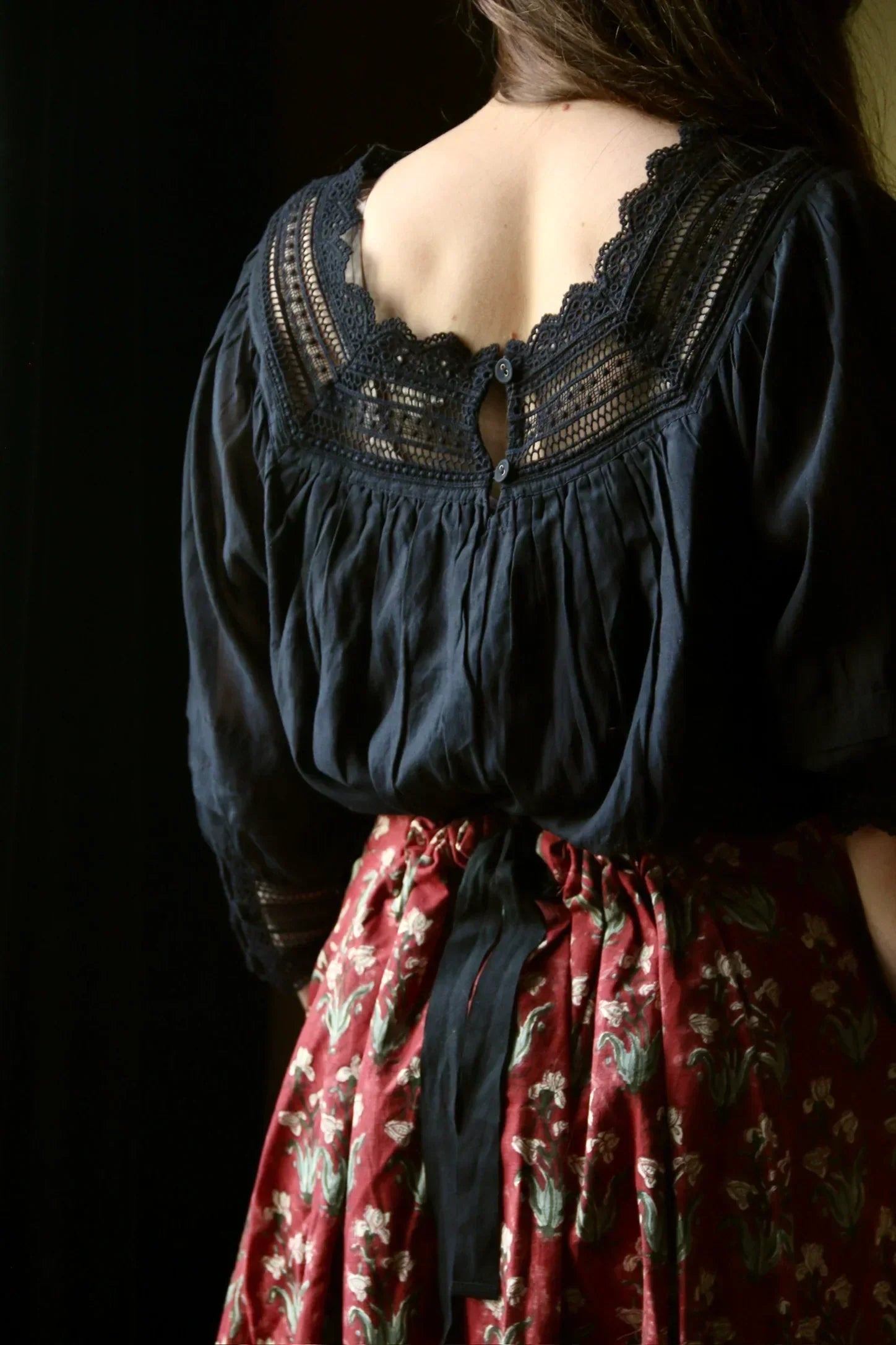 Woman in navy lace blouse and red floral skirt with bow, back view, soft lighting