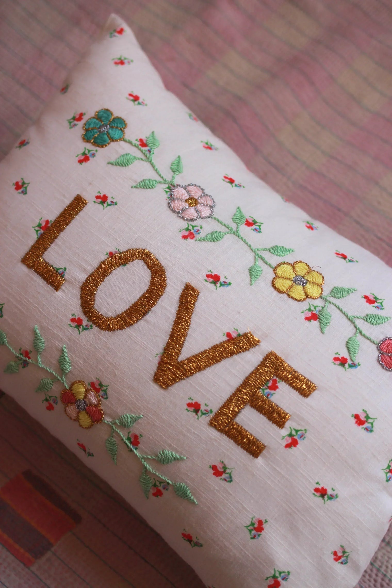 Embroidered linen cushion with floral details and gold "LOVE" lettering, on a striped fabric.