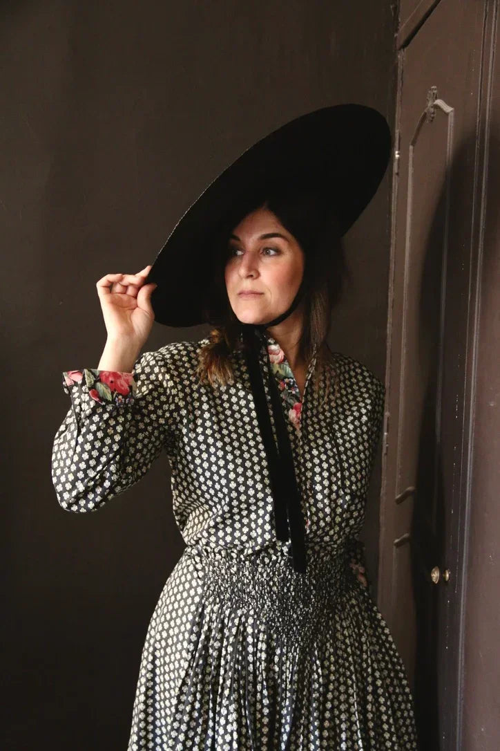 Woman in a vintage floral-patterned dress and large black hat with ribbon, indoors