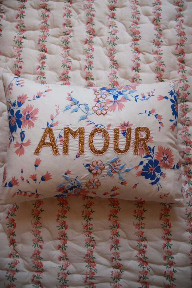 Decorative floral embroidered cushion with 'AMOUR' text on patterned quilt bedding