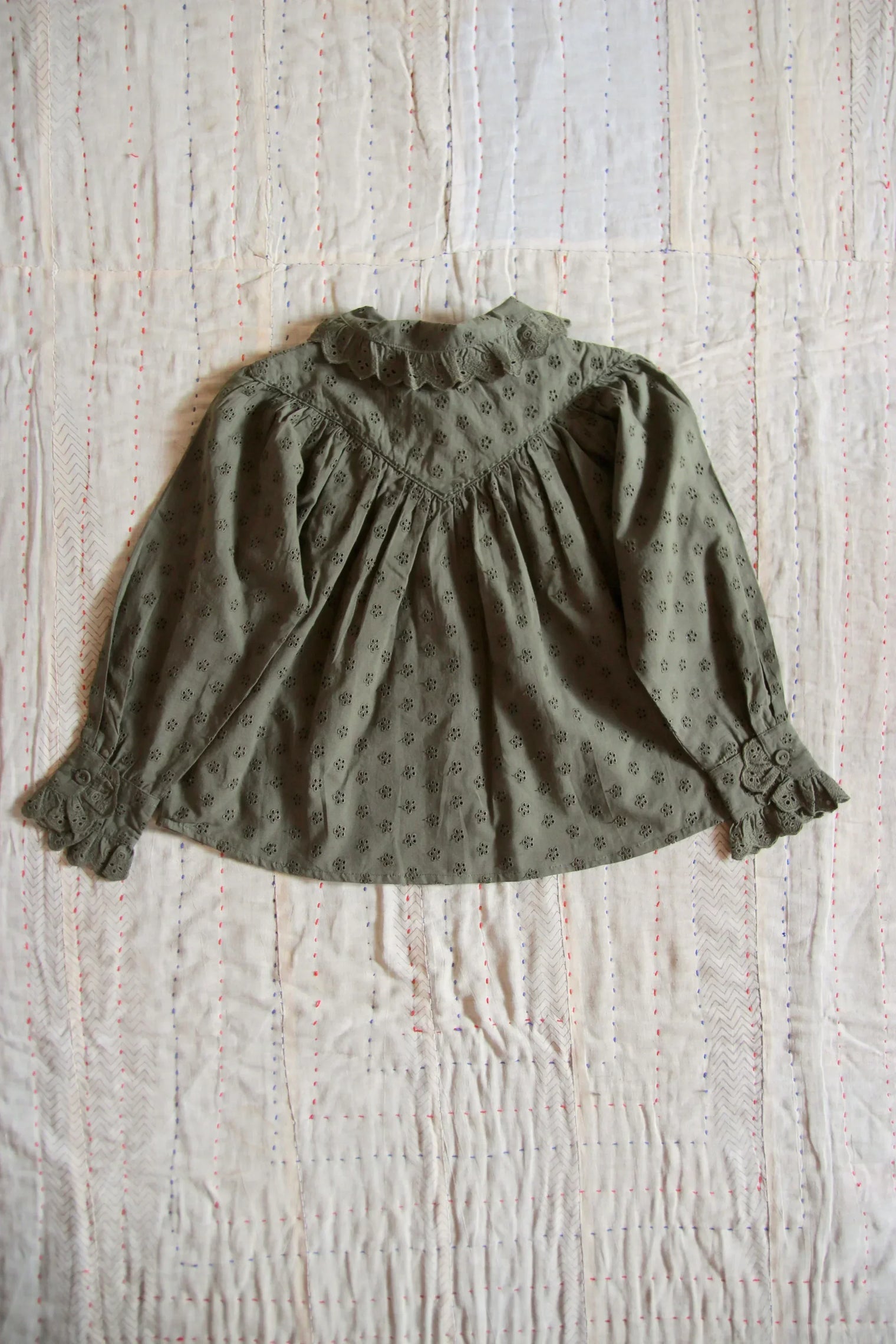 Green embroidered long sleeve children's blouse with lace collar on a quilted fabric background