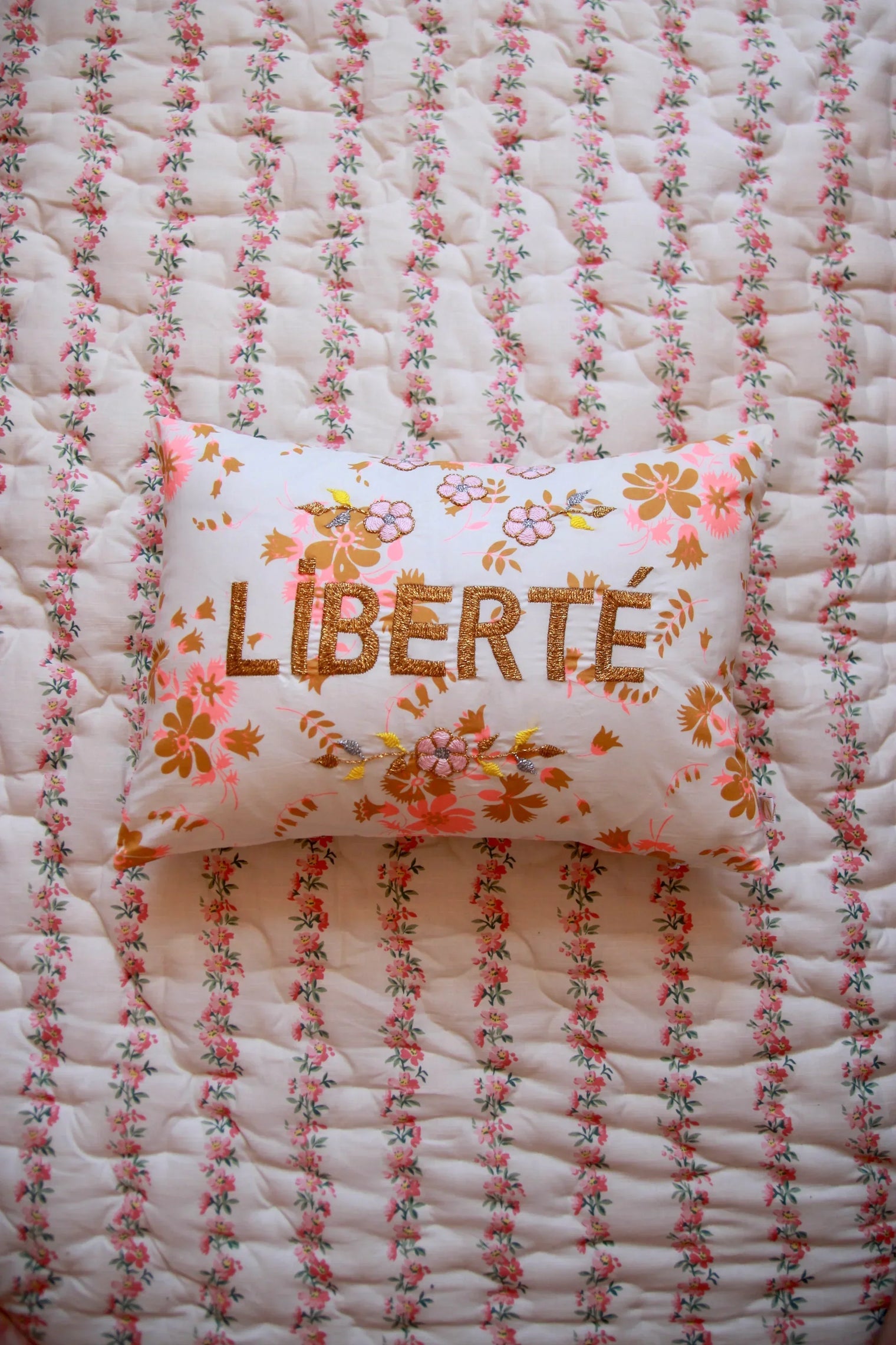 Floral embroidered pillow with 'LIBERTÉ' text on quilted, floral-print bedding