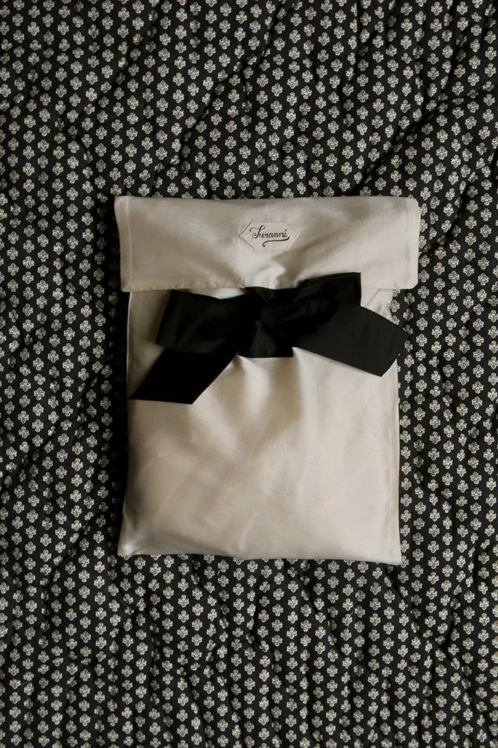Cream fabric pouch with black ribbon on quilted floral patterned bedding
