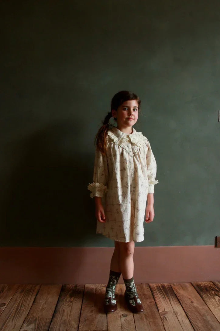 Girl in a vintage-inspired cream dress with a lace collar, standing on wooden floor