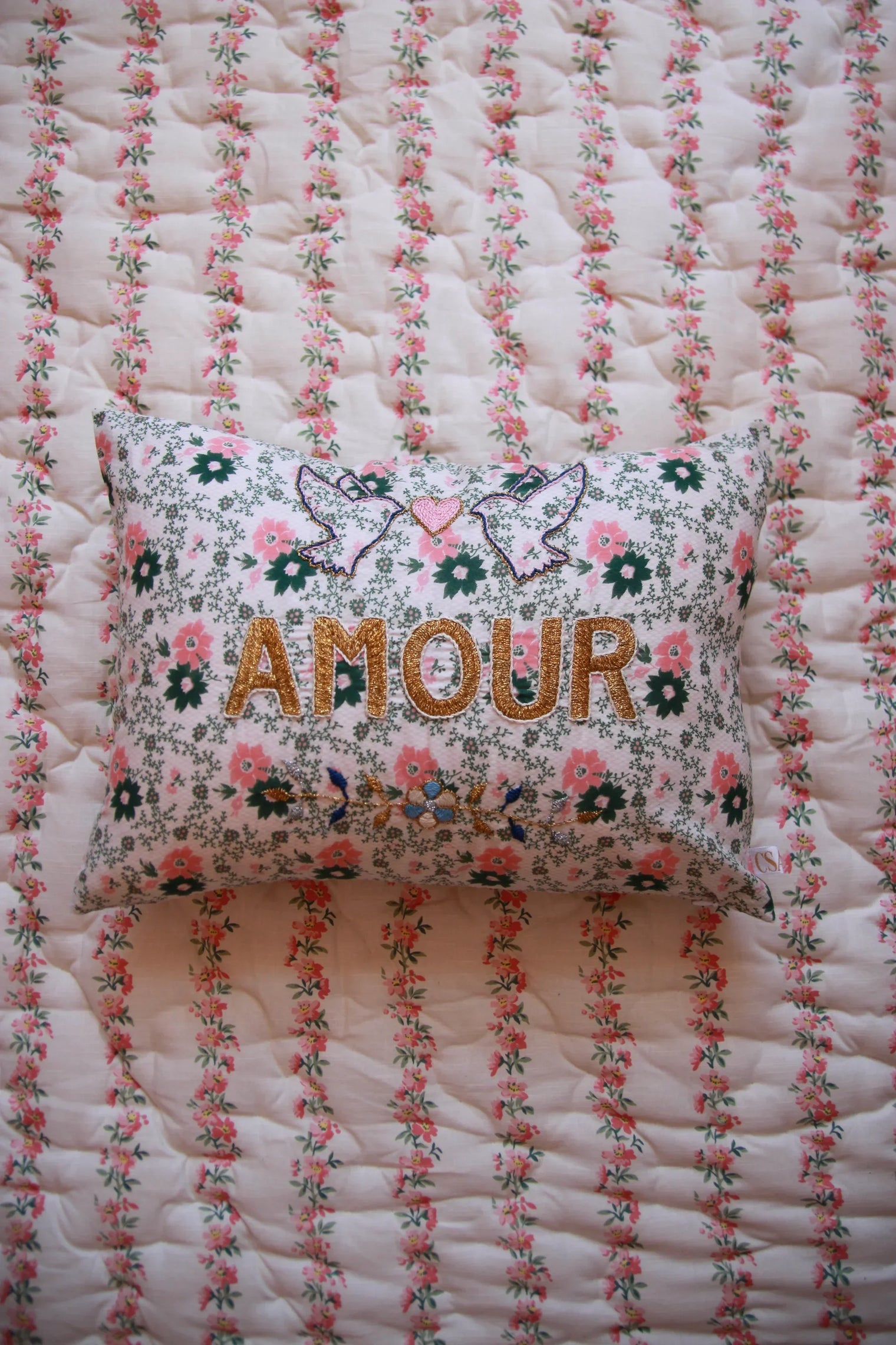 Floral embroidered pillow with 'AMOUR' text and doves on a quilted pink floral blanket
