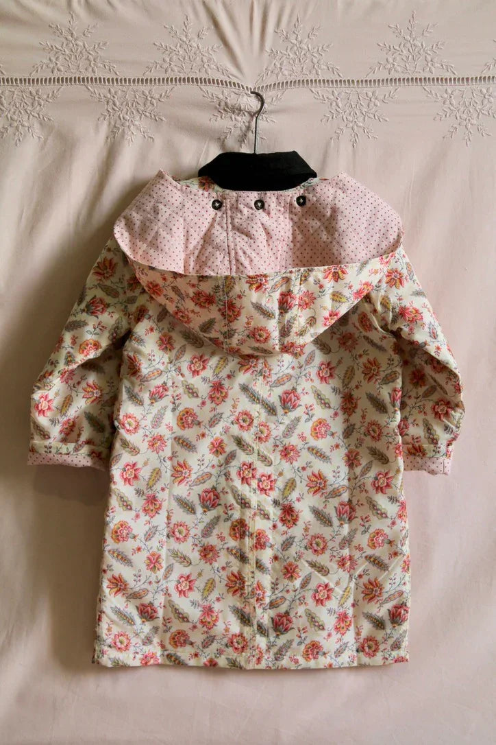 Children's floral print raincoat with hood, pastel pink and cream, hanging on a hanger.