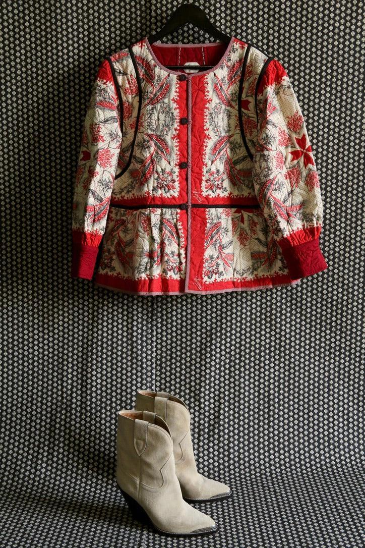Quilted floral jacket with red accents on hanger and beige suede ankle boots below