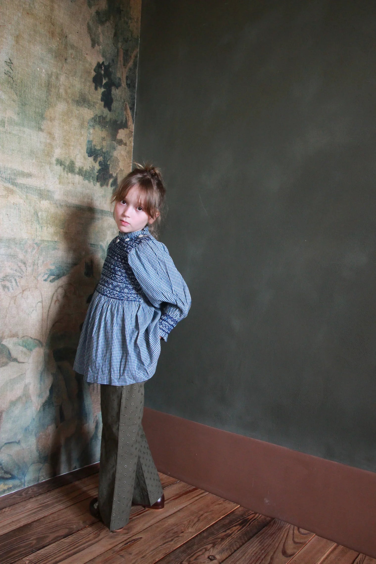 Girl in a vintage-inspired blue smock top and olive embroidered trousers indoors