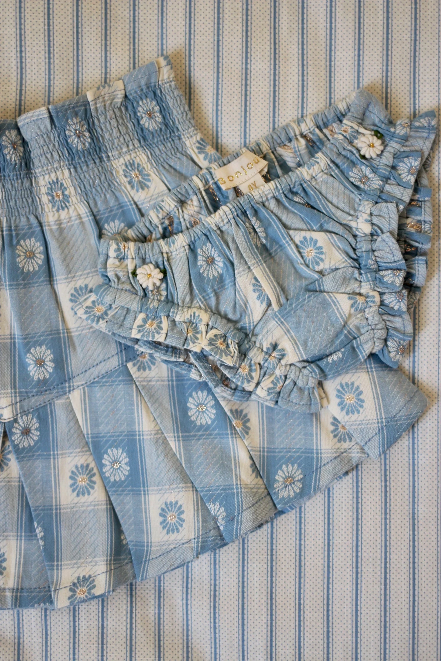 Blue floral checkered children’s skirt and bloomers with ruffles on striped linen background