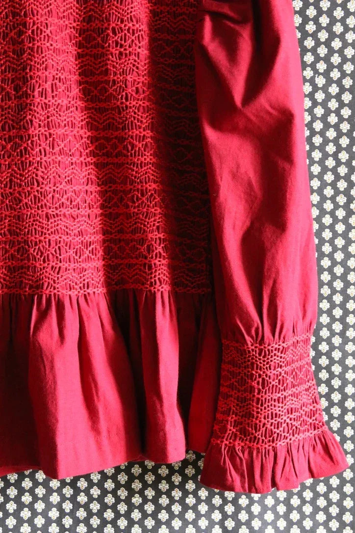 Red long sleeve blouse with lace smocking details, ruffled hem and cuff, patterned background