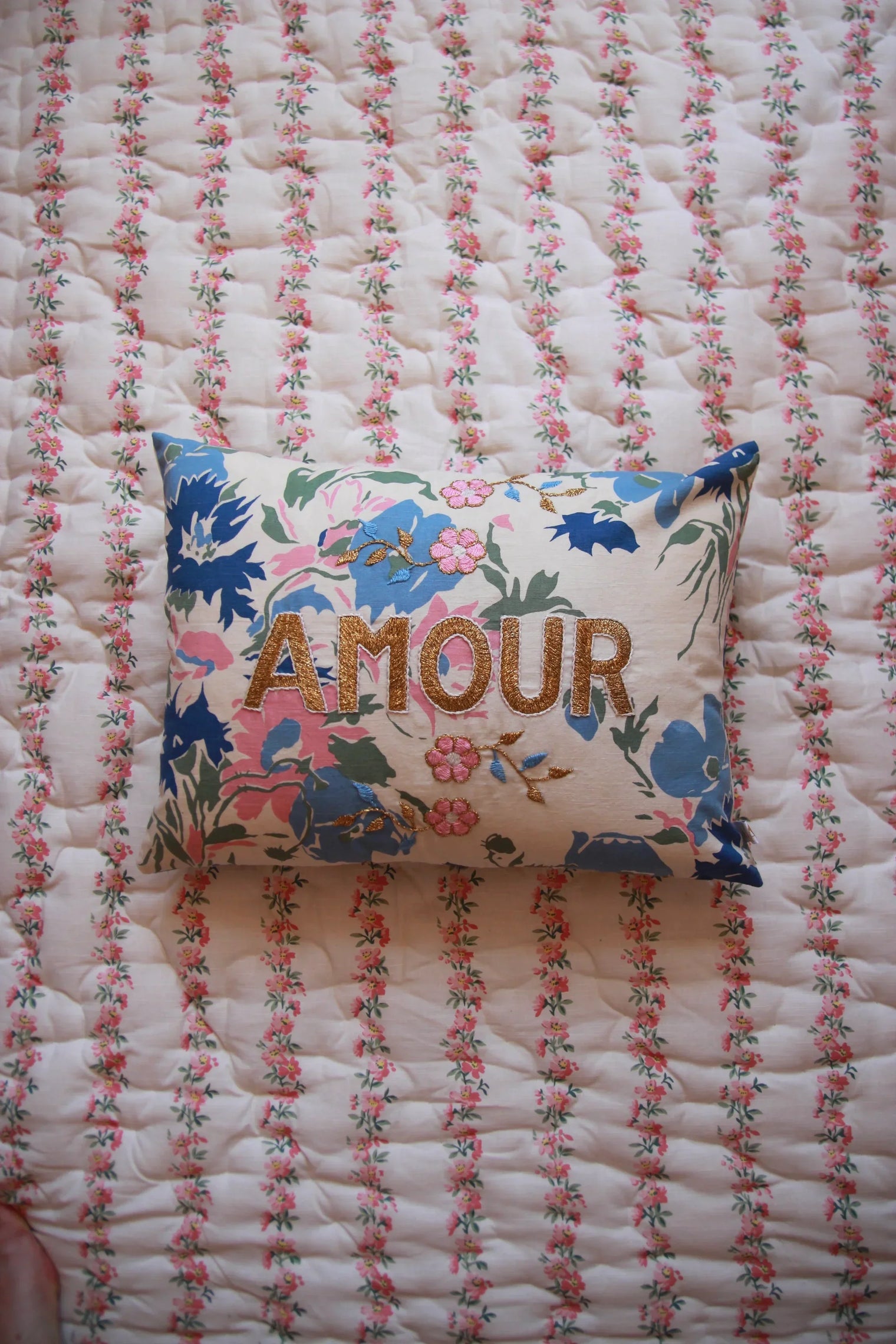 Floral embroidered cushion with "AMOUR" text on a pink floral quilt, decorative home linen