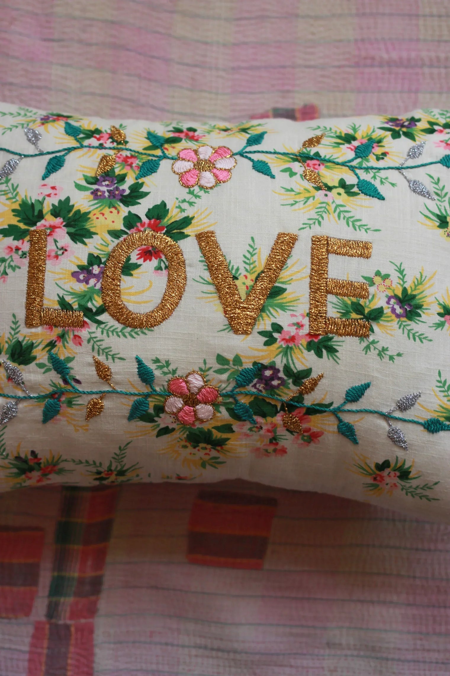 Floral embroidered pillow with gold 'LOVE' text on a pastel quilt