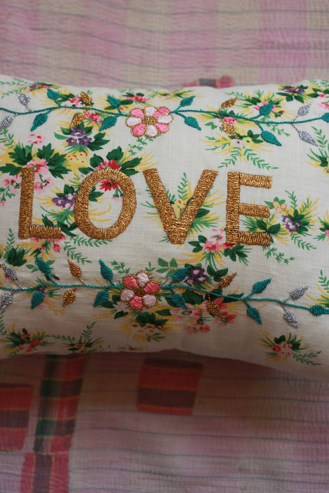 Floral embroidered pillow with gold 'LOVE' text on a pastel quilt