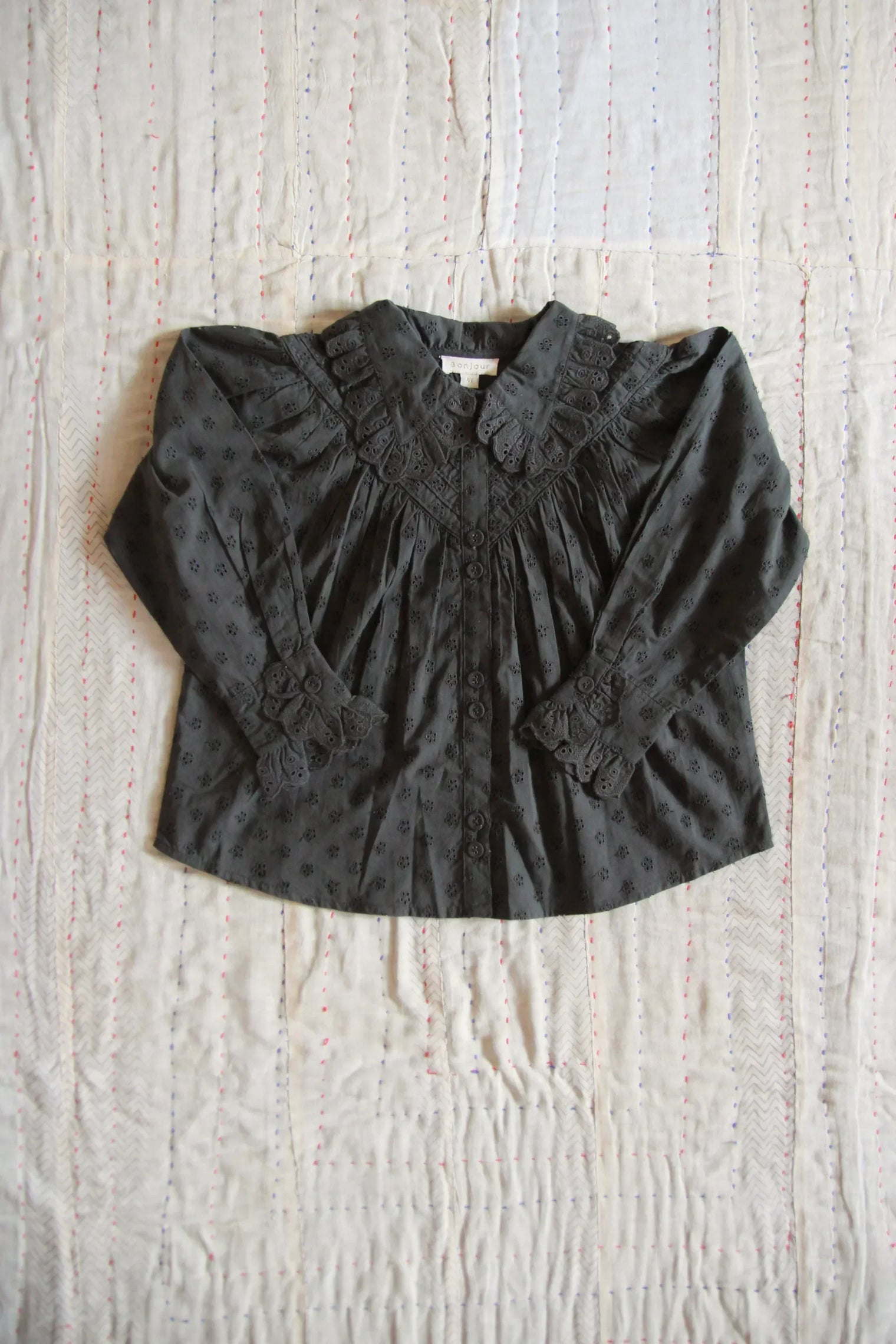 Black long sleeve children's blouse with lace collar and cuffs on a quilted background