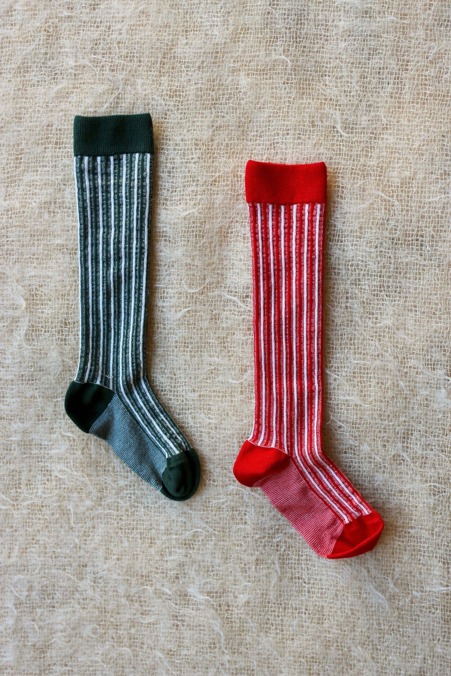 Two pairs of striped knee-high kids' socks, one green and one red, on textured fabric