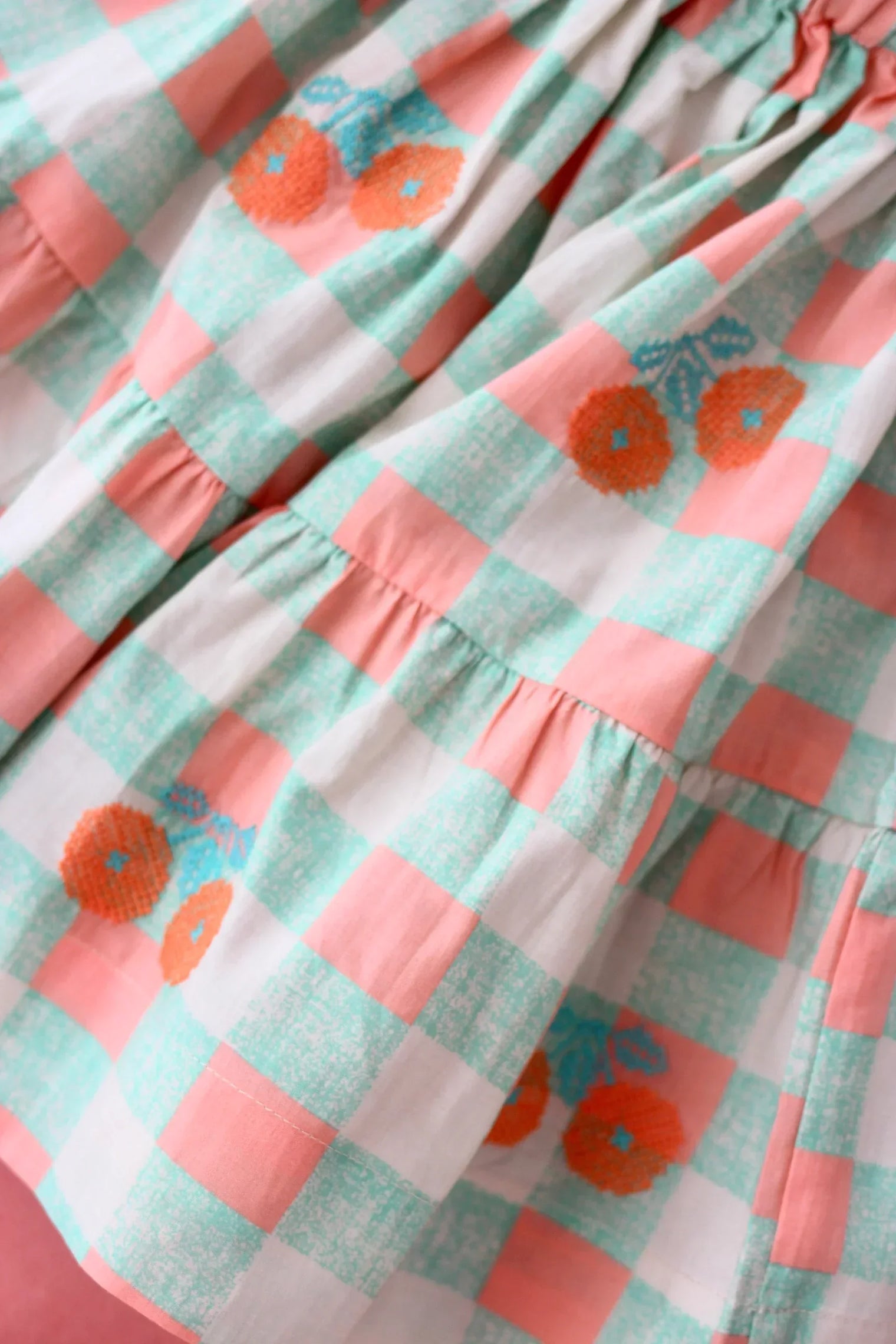 Close-up of a pastel pink and mint green gingham dress with orange floral embroidery