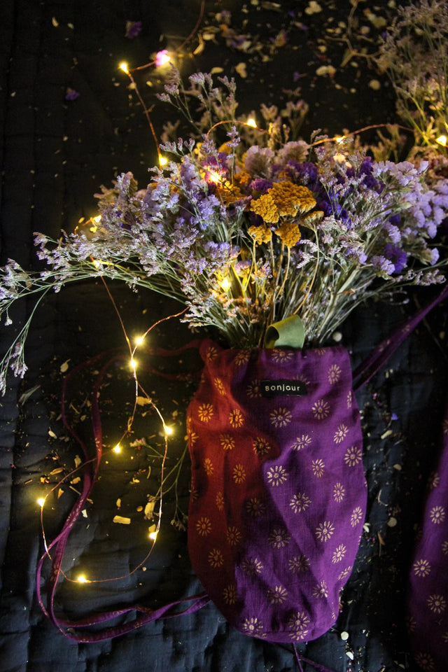 Purple floral drawstring pouch with dried flowers and string lights on dark fabric